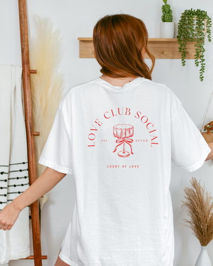 Person wearing a white t-shirt with red text and design in a room with decor elements.